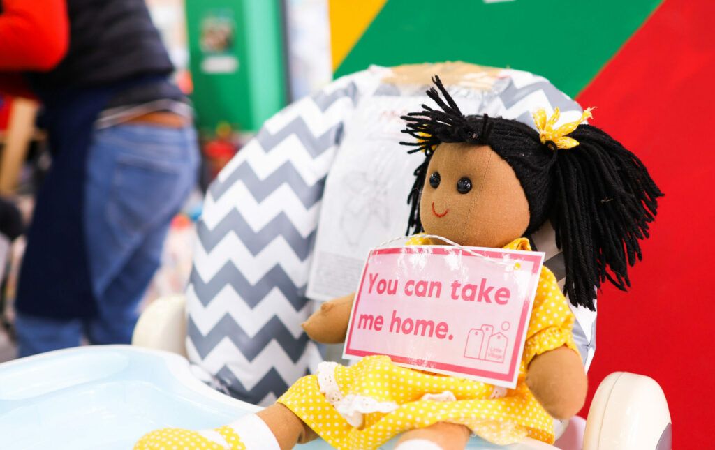 Image of a doll with a 'You can take me home' sign