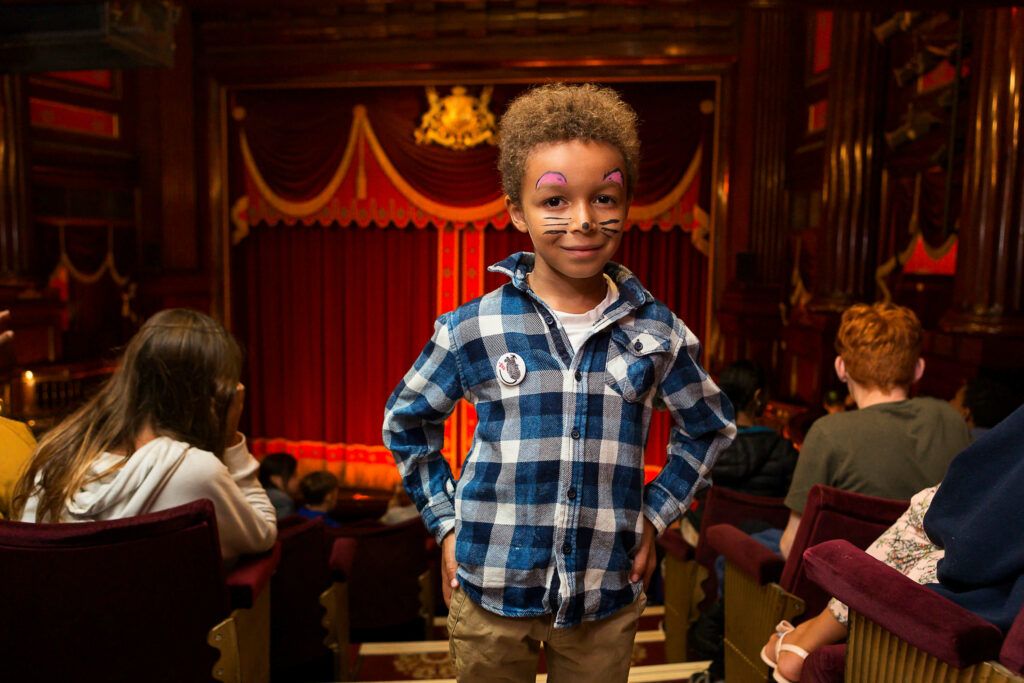 a young boy with face paint standing in the aisle of a theatre