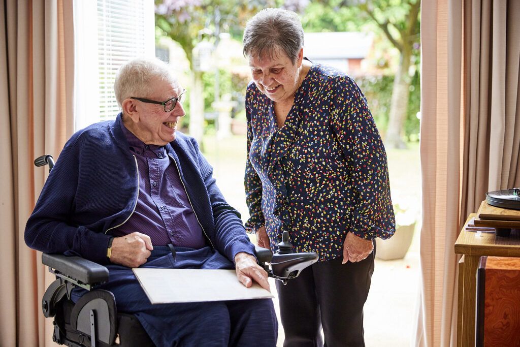 Carers UK - elderly man in a wheelchair smiling with an elderly lady.