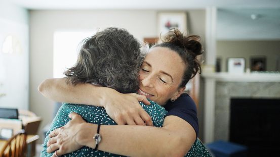Over the shoulder view of a young woman smiling while giving her mother a big hug after arriving back home for a visit