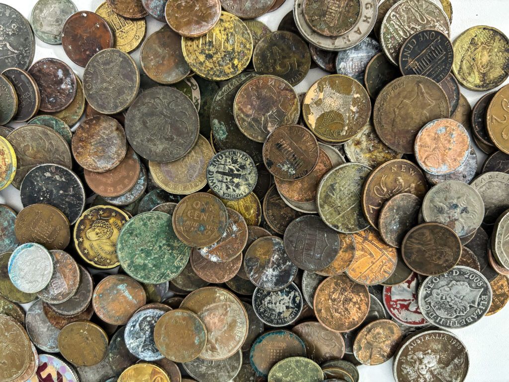 Pile of coins from around the world that have water damage and corrosion.